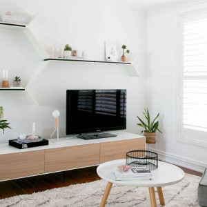 تزیین دیوار پشت تلویزیون با شلف دیواری سفید و مدرن که قاب عکس و گلدان روی آن قرار دارد
