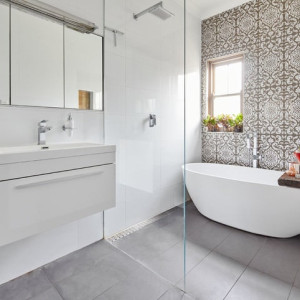 حمام مدرن با روشویی کابینت دار سفید و دیوار تاکیدی با کاشی های طرح دار و وان جزیره